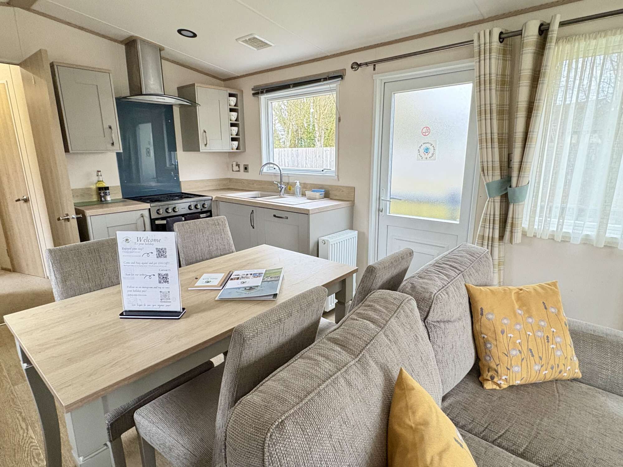 A compact kitchenette with a stove, sink, and cabinets, a dining table with a menu, and a sofa with a cushion.