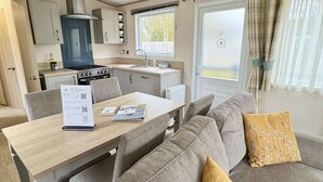 A compact kitchenette with a stove, sink, and cabinets, a dining table with a menu, and a sofa with a cushion. - Relax with the whole family at this peaceful place to stay (Hoburne Holiday Park)