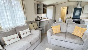 A compact living space with two grey sofas, a wooden coffee table, and a kitchenette in the background. - Relax with the whole family at this peaceful place to stay (Hoburne Holiday Park)