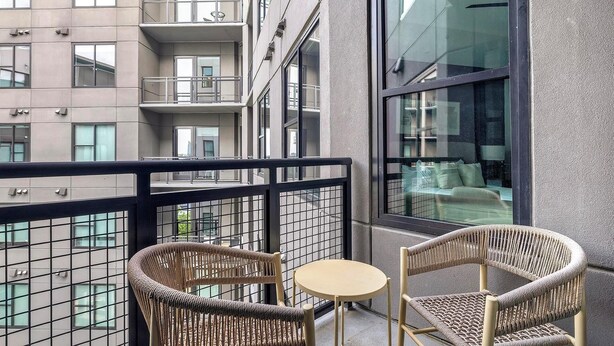 Ein Balkon mit Korbstühlen und einem kleinen runden Tisch, mit Blick auf ein Gebäude mit zahlreichen Fenstern und Balkonen.