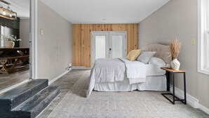 A bedroom with a bed, bedside table, and a view of a hallway with a staircase.