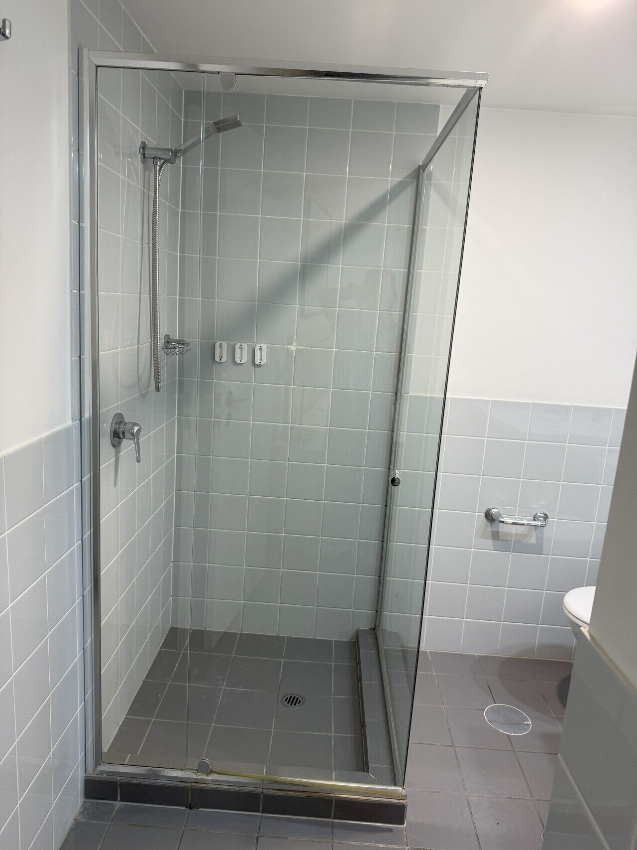 A glass-enclosed shower with a handheld showerhead and a wall-mounted faucet.