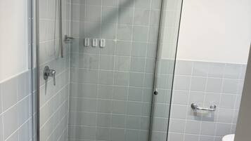A glass-enclosed shower with a handheld showerhead and a wall-mounted faucet.