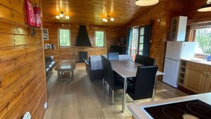 A wooden cabin interior with a dining area, kitchen, and a fireplace. - Bumble Bee Cabin on Heron Lake (Hoburne Holiday Park)
