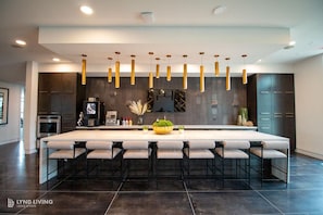 A modern kitchen with a large island, bar stools, dark cabinetry, and pendant lighting. - Landing | Stunning 1BD, Clubhouse, Pool (San Antonio)