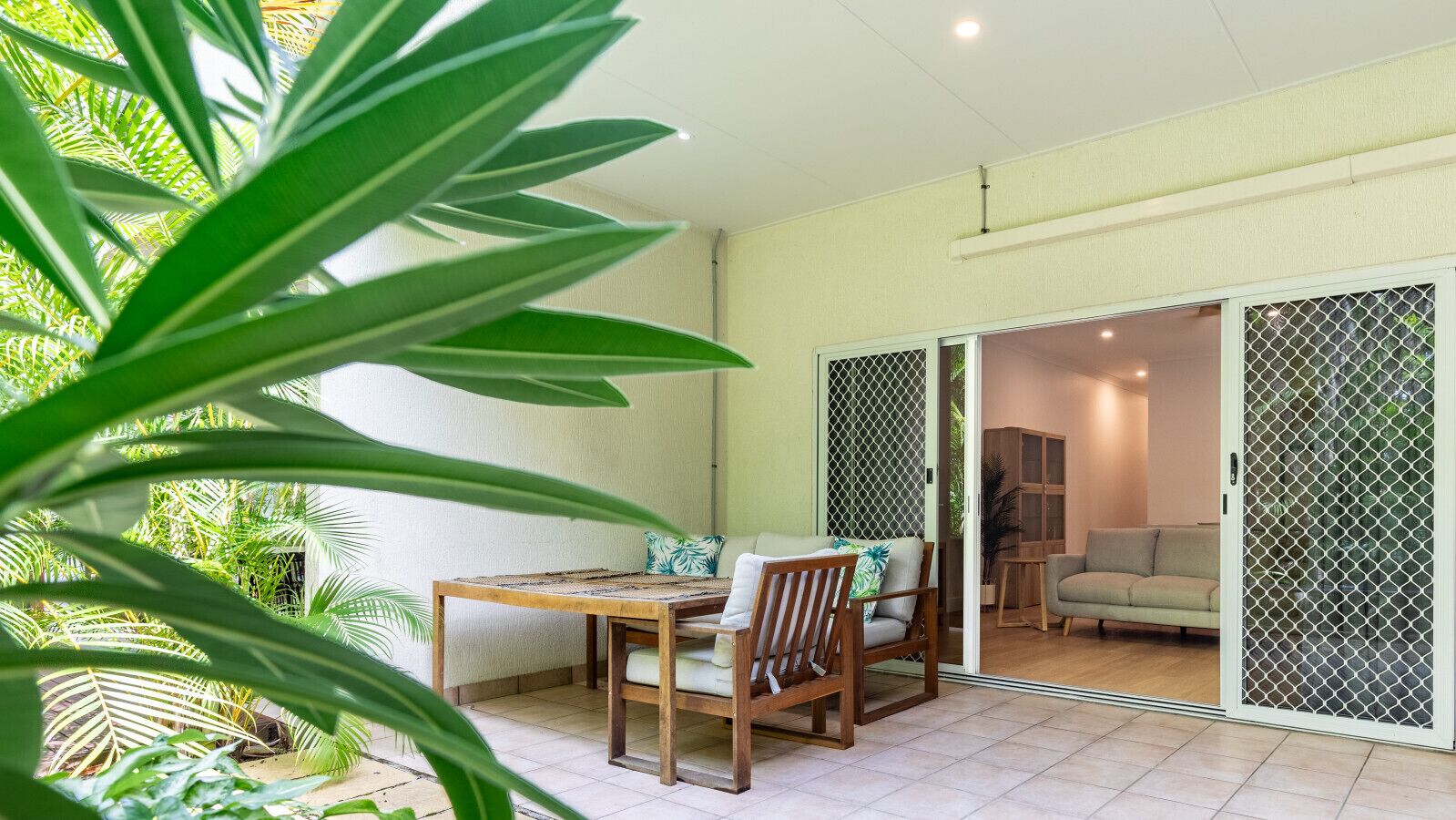 A room with a sliding glass door leading to a balcony, a wooden table with chairs, and a sofa.