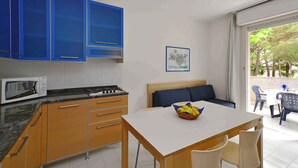 Una cocina compacta con armarios azules, un microondas y una estufa. Hay un comedor con mesa y sillas, y un sofá.