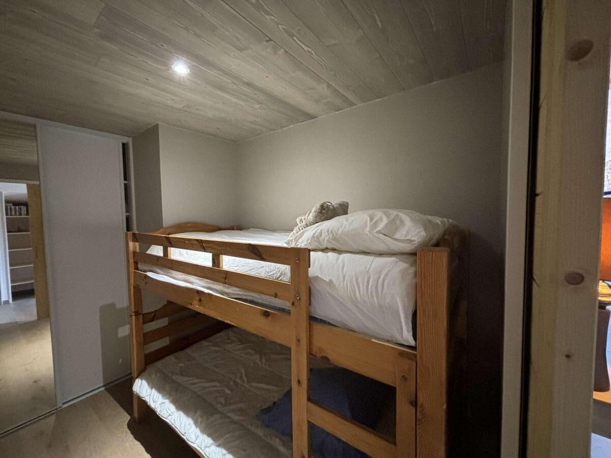 Een stapelbed in een kamer met een houten plafond en een witte deur.