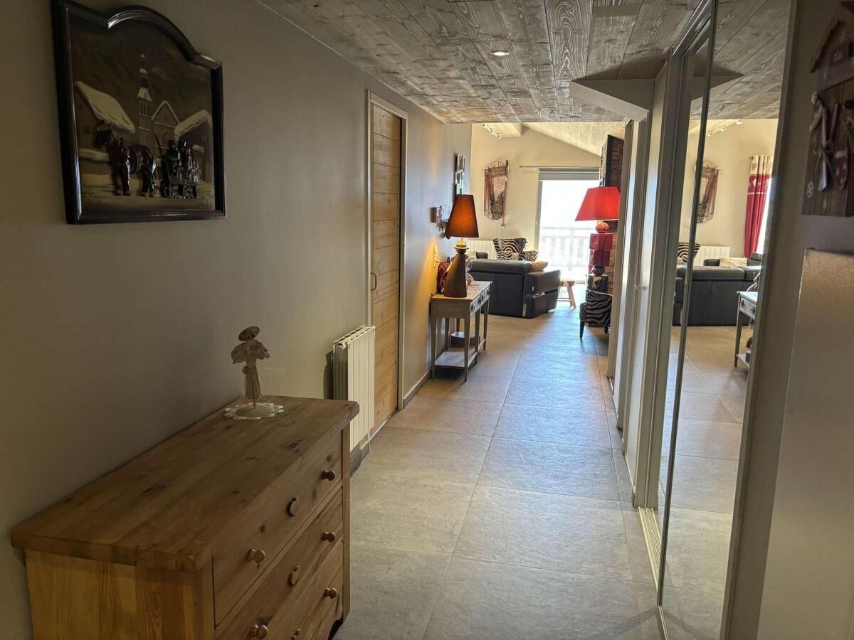 Ein schmaler Flur mit einem Holzkleiderschrank, einem Heizkörper und einer Lampe. An der Wand hängt ein Gemälde und es gibt ein Fenster mit Vorhängen.