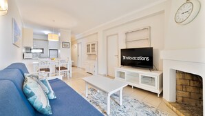 Ein Wohnzimmer mit einer Couch, einem Couchtisch, einem Fernseher, einem Kamin und einer Küche im Hintergrund.