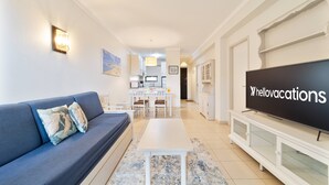 Ein modernes Wohnzimmer mit Sofa, Couchtisch, Fernseher und einer Küche im Hintergrund.