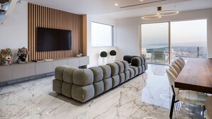 Una sala de estar moderna con un televisor de pantalla plana grande, un sofá seccional, una mesa de comedor y vistas de la ciudad.
