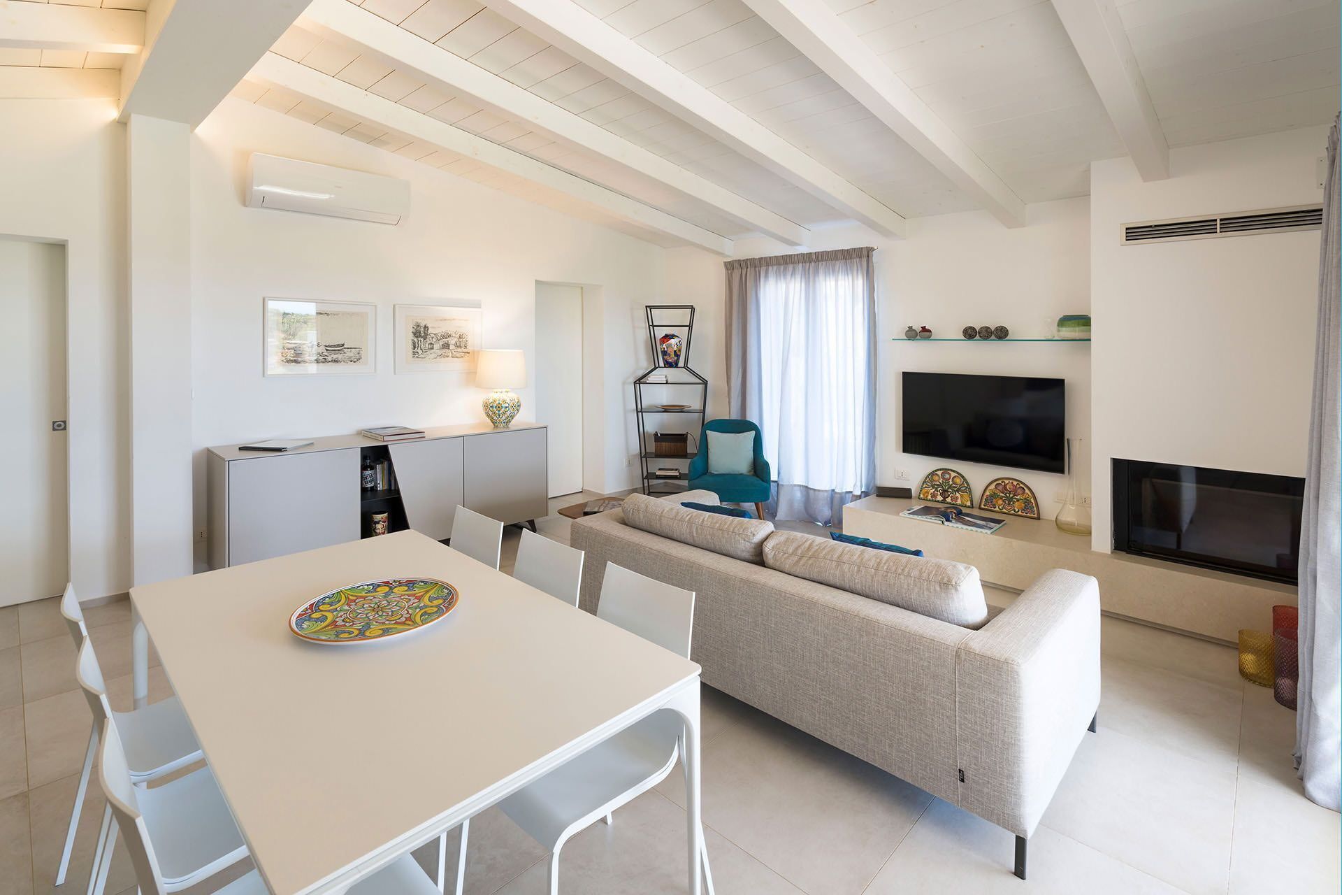 Una sala de estar moderna con un sofá, una mesa de comedor y sillas. Hay un televisor montado en la pared y una chimenea.
