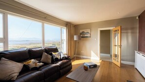 A spacious living room with a leather sofa, a coffee table, and a view of a landscape through large windows.