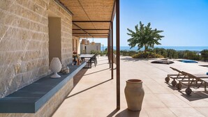 A covered outdoor area with a stone wall, a table with chairs, a large vase, and a view of the sea. - Villa Miriam with swimming pool - My Rental Homes (Scicli)