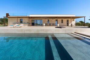 Een modern huis met een zwembad, een terras met lounge stoelen en een overdekt buitengebied.