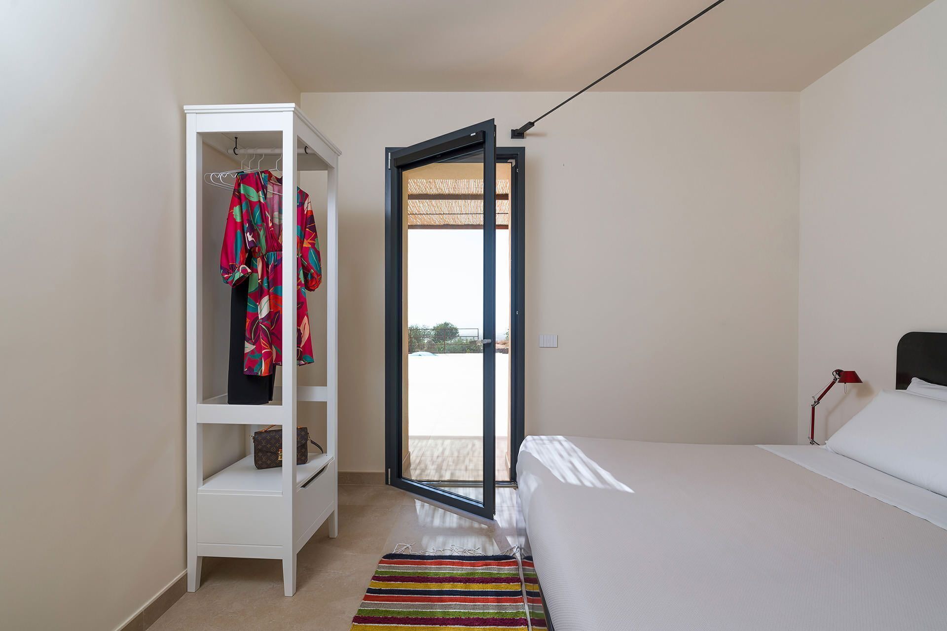 A bedroom with a bed, a wardrobe, and a sliding glass door leading to a balcony.