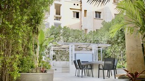 Un espace extérieur aménagé en patio, avec une pergola blanche, un coin salon et une végétation luxuriante.