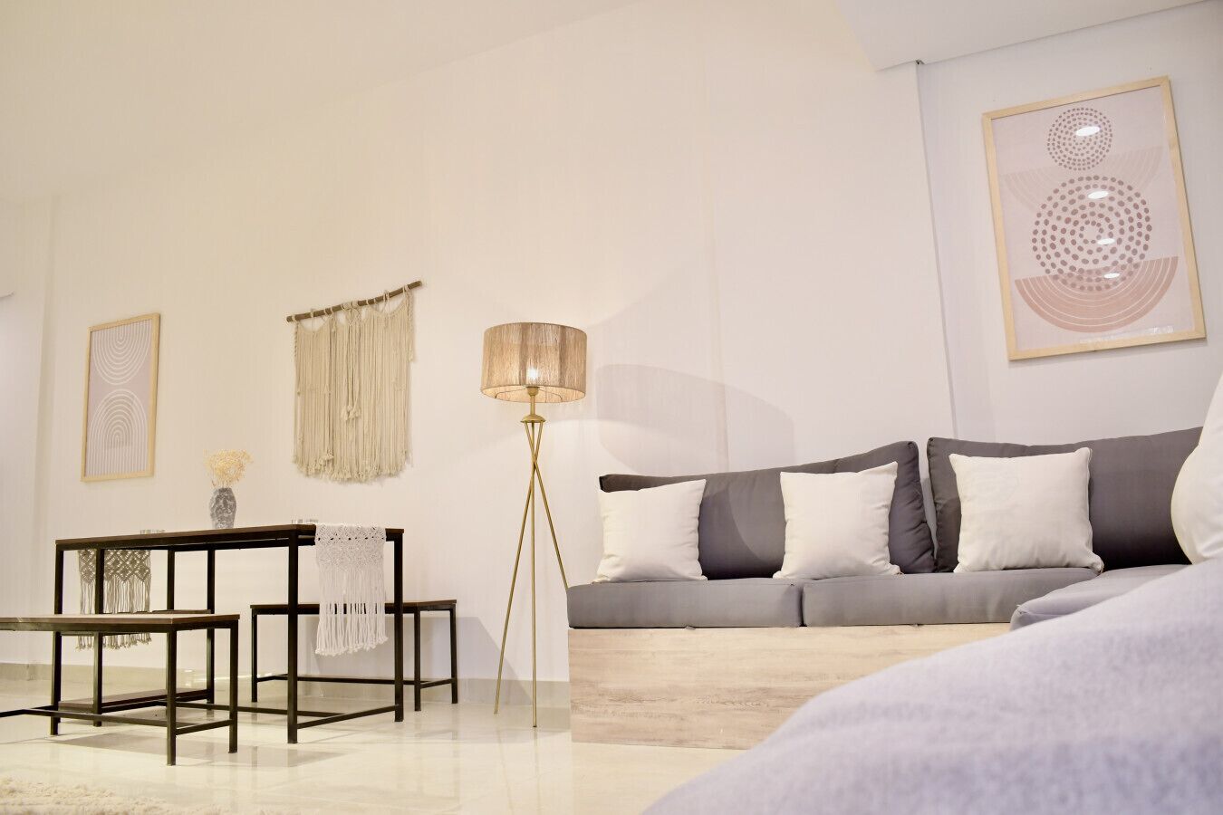 Un salon moderne avec un canapé gris, une petite table, une lampe sur pied et des œuvres d’art murales.