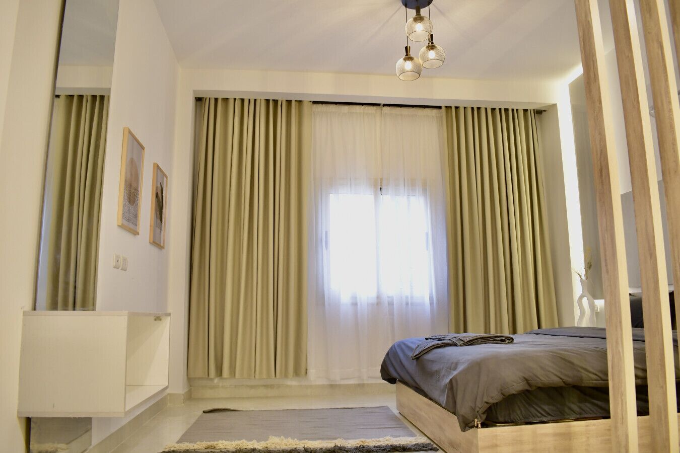 A bedroom with a bed, a bedside table, a mirror, and a window with curtains.