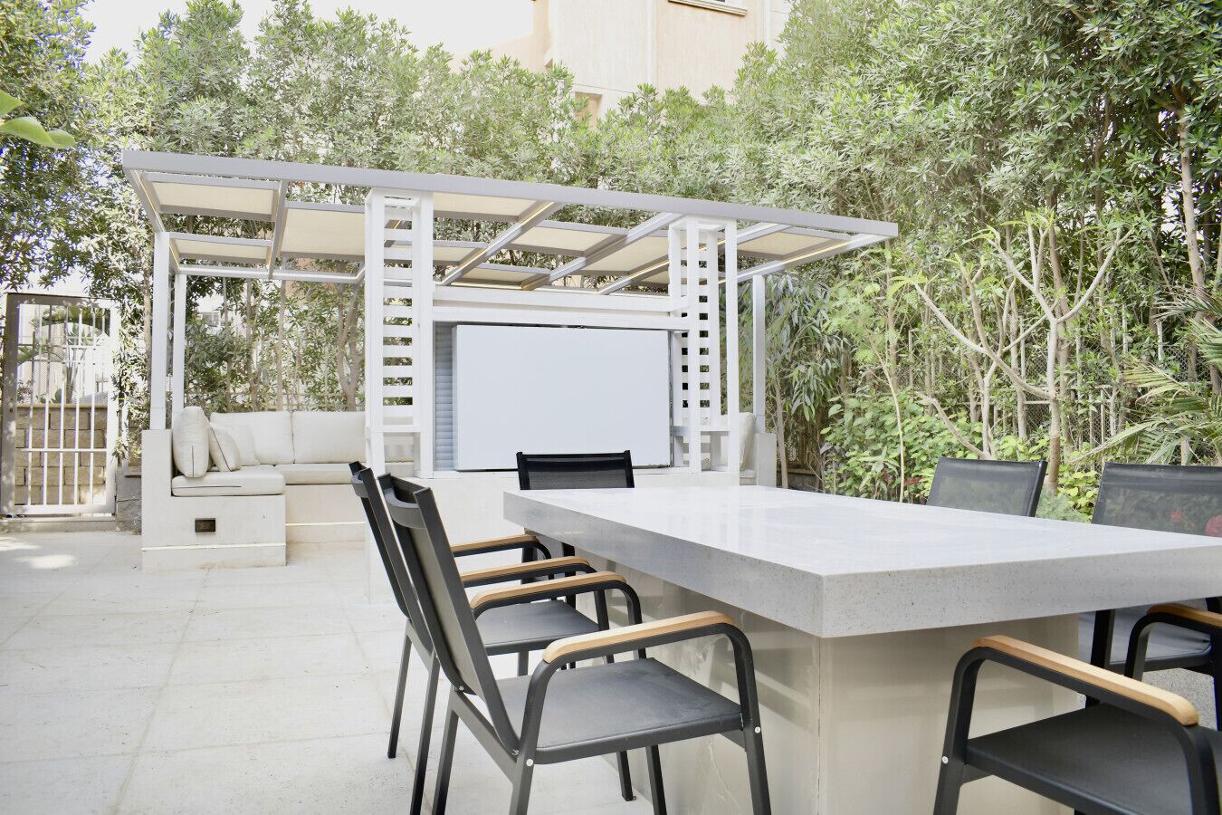 Un espace extérieur aménagé en terrasse, avec une table et des chaises blanches, un canapé blanc et une structure en forme de pergola.