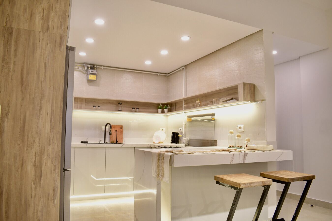 Una cocina moderna con encimera de mármol, horno integrado y un taburete de madera.