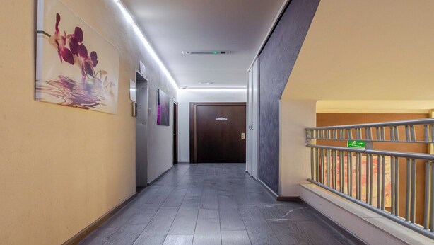 A corridor with a wooden floor, a painting on the wall, and a door at the end.