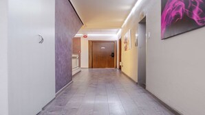 A hotel corridor with a wooden floor, a door at the end, and a wall-mounted artwork.