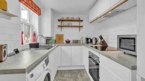 A modern kitchen with white cabinetry, a built-in oven, a microwave, and a sink. - Mill Cottage | By My Getaways (Brighton)