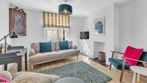 A modern living room with a sofa, a dining table, a TV, and a window with blinds. - Mill Cottage | By My Getaways (Brighton)