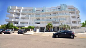 Un edificio de varios pisos con balcones, estacionamiento y una palmera.