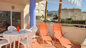 A terrace with a table set for two, two white chairs, and two orange lounge chairs. - Apartment in Roses with large terrace (Rosas / Roses)