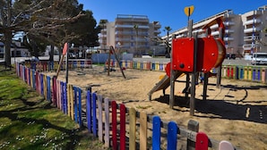 A playground with a red slide and swings, surrounded by a colorful fence. - Apartment in Roses with large terrace (Rosas / Roses)