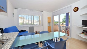 A modern room with a glass table, blue chairs, a kitchen area, and a balcony with outdoor furniture. - Apartment in Roses with large terrace (Rosas / Roses)