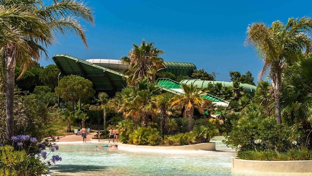 A resort pool area with palm trees, a water slide, and a building with a green roof. - Apartment in Roses with large terrace (Rosas / Roses)