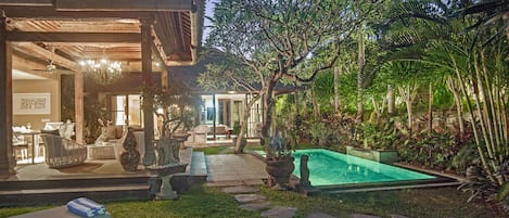 A traditional house with a swimming pool, outdoor seating, and lush greenery.