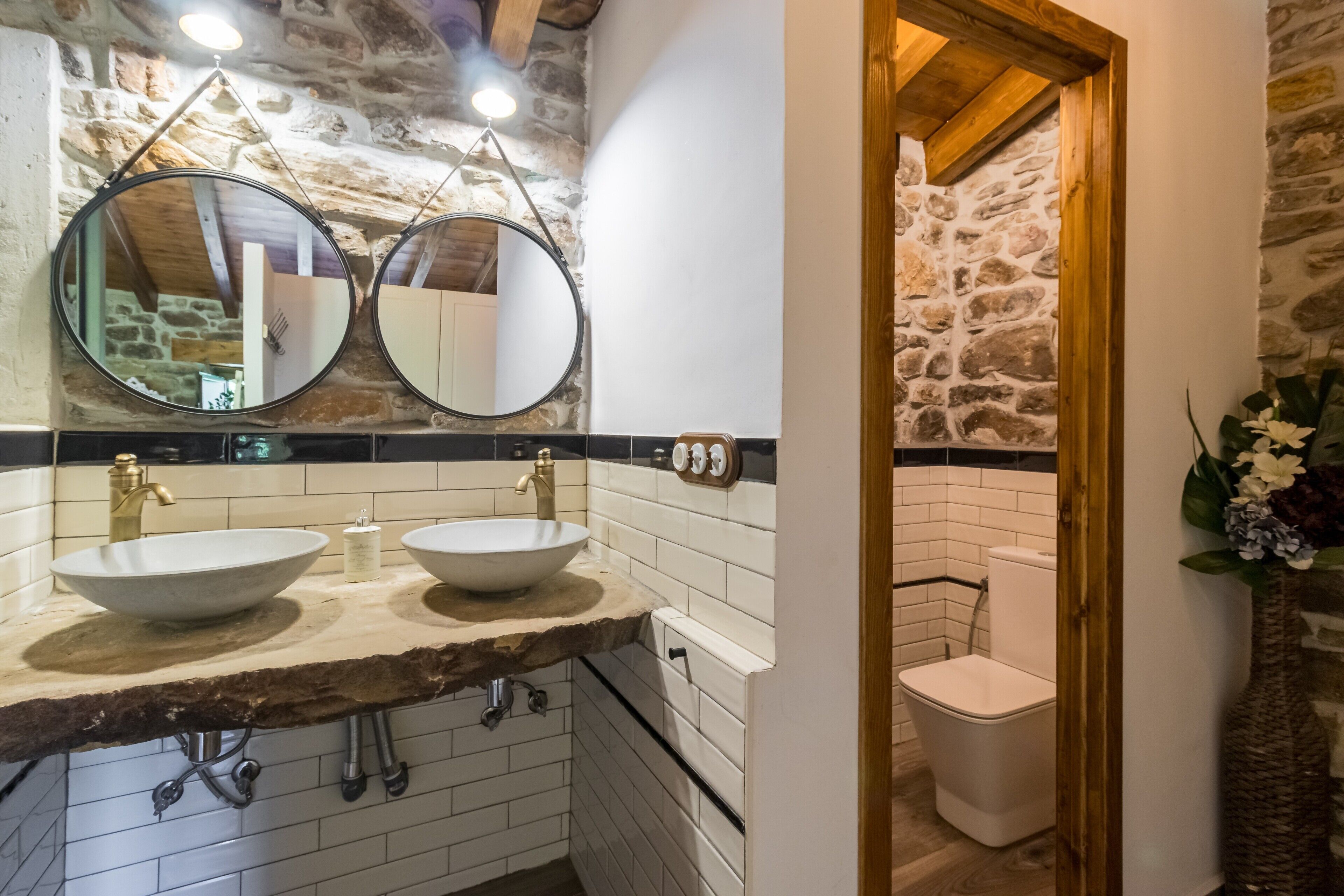 A bathroom with two sinks, a stone wall, and a wooden door.