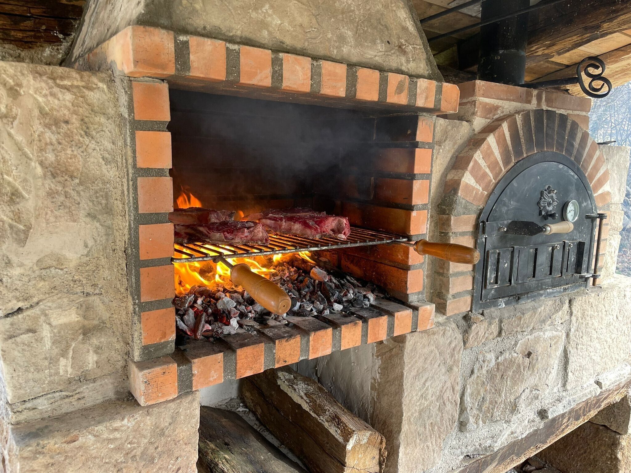 Parrilla de ladrillo con carne asándose, un termómetro y una chimenea.
