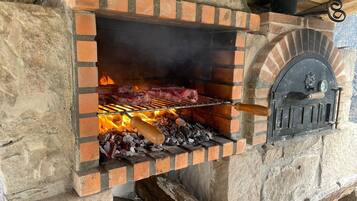 Parrilla de ladrillo con carne asándose, un termómetro y una chimenea.