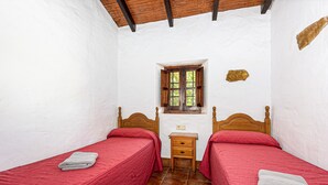 A room with two beds, a small wooden nightstand, a window, and a white wall.