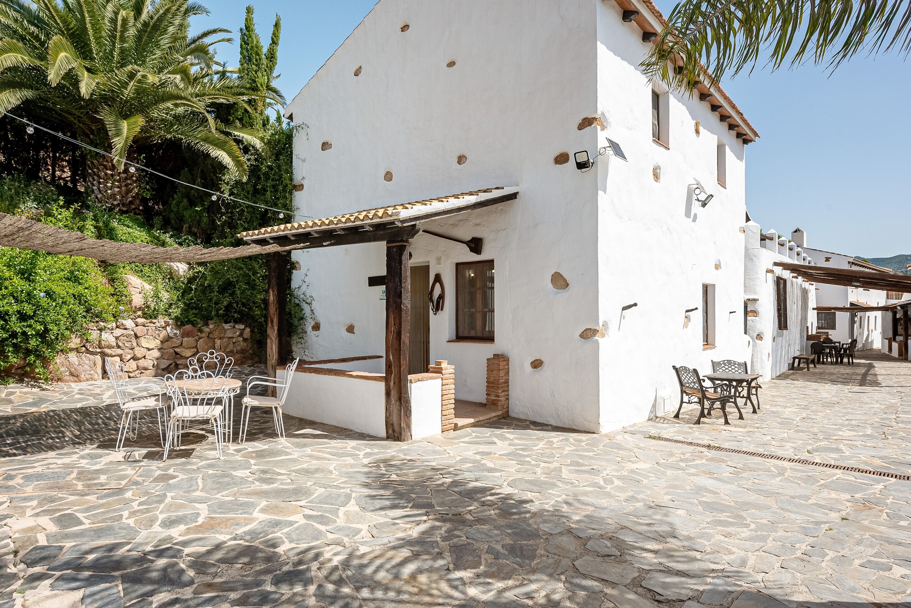 A white building with a stone patio, outdoor seating, and a palm tree.