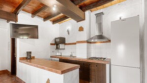 A kitchen with a central island, a stove, a microwave, a refrigerator, and wooden beams on the ceiling.