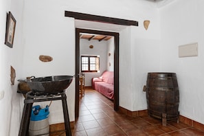 Un pasillo estrecho con una estufa, una olla grande, un cilindro de gas azul y un barril de madera.
