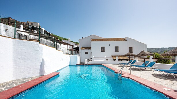 A swimming pool with a red border, a white building with a tiled roof, and blue lounge chairs. - Country House 'La Casa Grande' with Lake View, Shared Pool and Wi-Fi (Málaga)