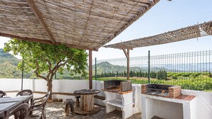 An outdoor patio with a grill, stone flooring, and a view of the countryside. - Country House 'La Casa Grande' with Lake View, Shared Pool and Wi-Fi (Málaga)