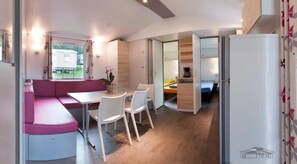 Una habitación compacta con kitchenette, un comedor con mesa y sillas, y una zona de estar con sofá rosa.
