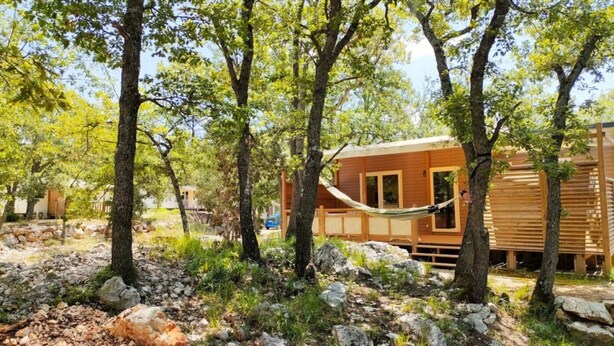 Una cabana de fusta envoltada d'arbres i roques, amb una hamaca penjada entre dues plantes.