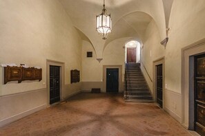Un couloir avec un escalier, une voûte et un luminaire suspendu.