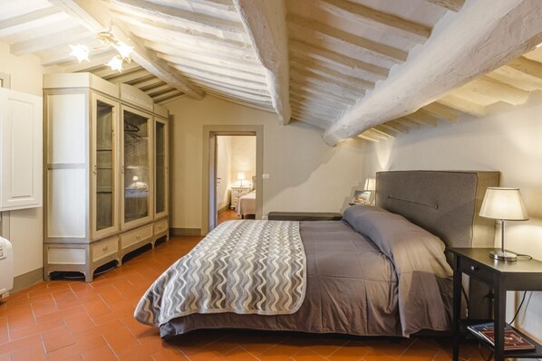 A bedroom with a bed, bedside table, lamp, wardrobe, and a ceiling with exposed beams.