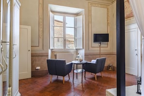 A room with a large window, two chairs, a small table, and a television mounted on the wall.